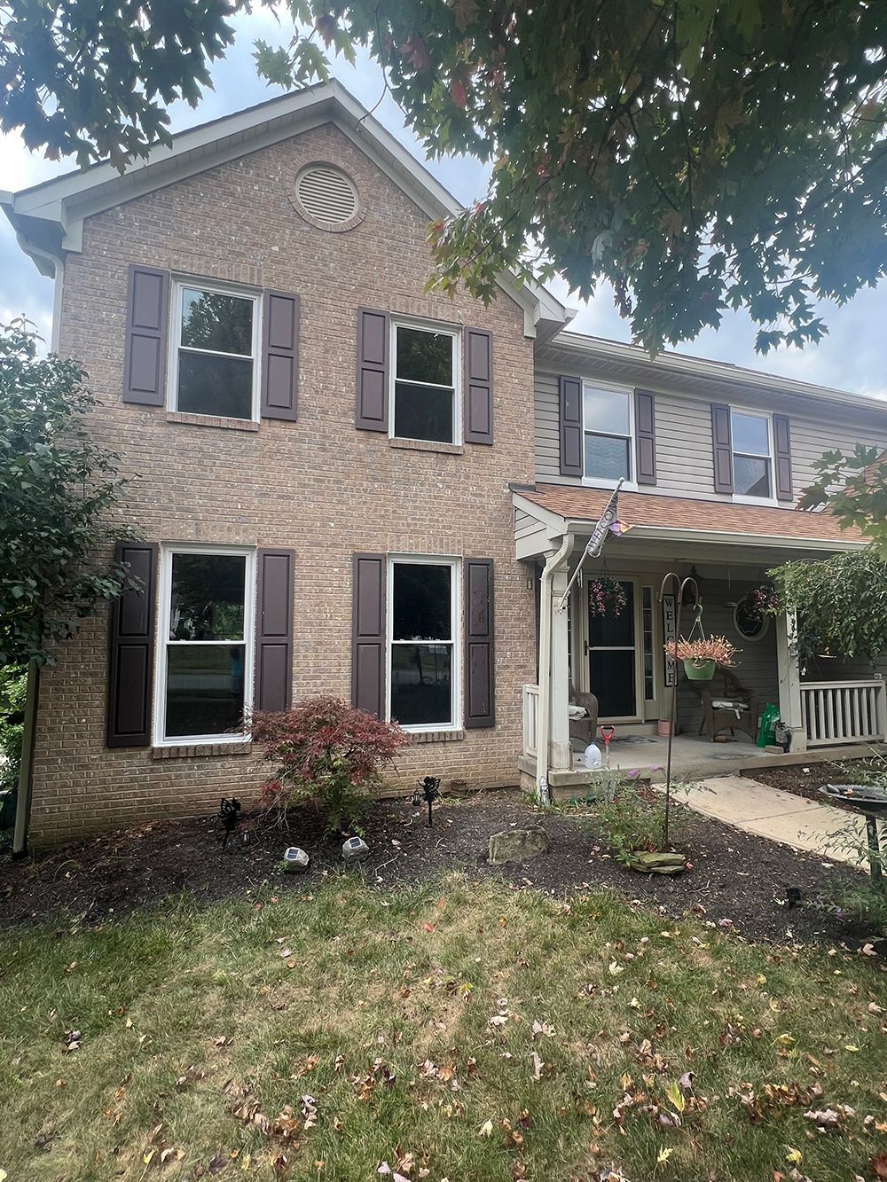 Two-story brick house with brown shutters, white-trimmed windows, and a covered porch.