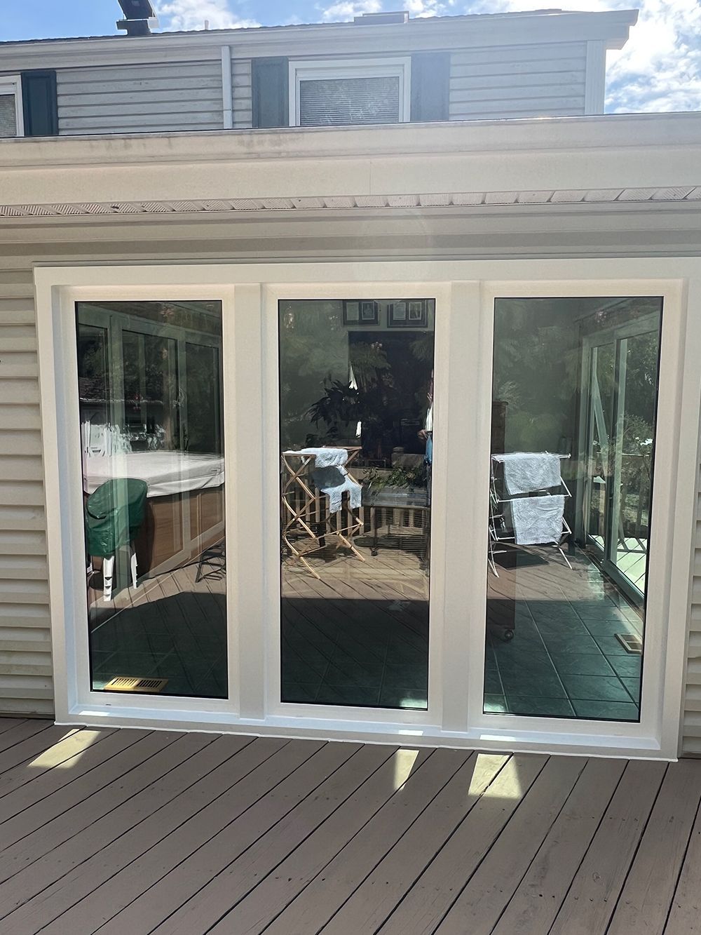 Three-pane window, white frame, reflecting a backyard with a hot tub, patio furniture, on a deck.