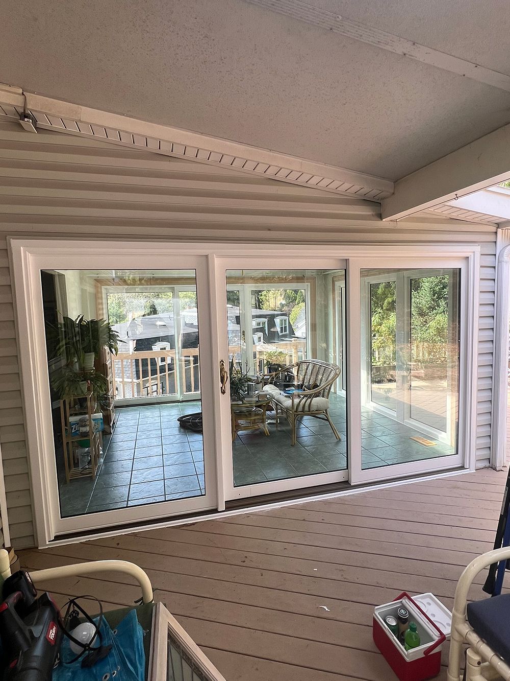 White framed sliding glass doors on a wooden deck, reflecting an interior with furnishings and greenery.