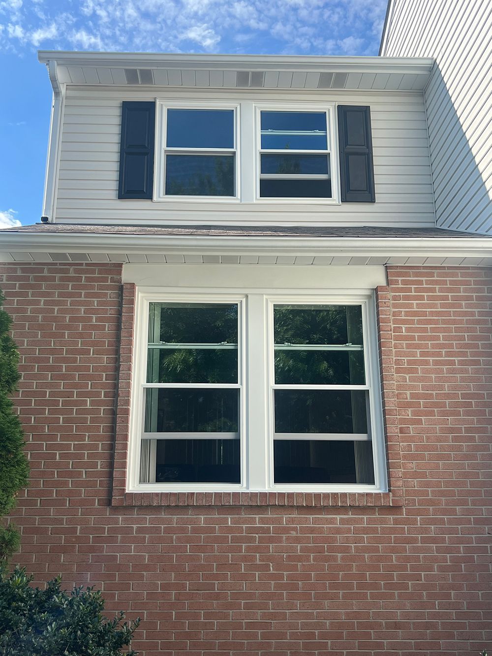 Two-story building with brick siding and white framed windows. Upper level has white siding and black shutters.