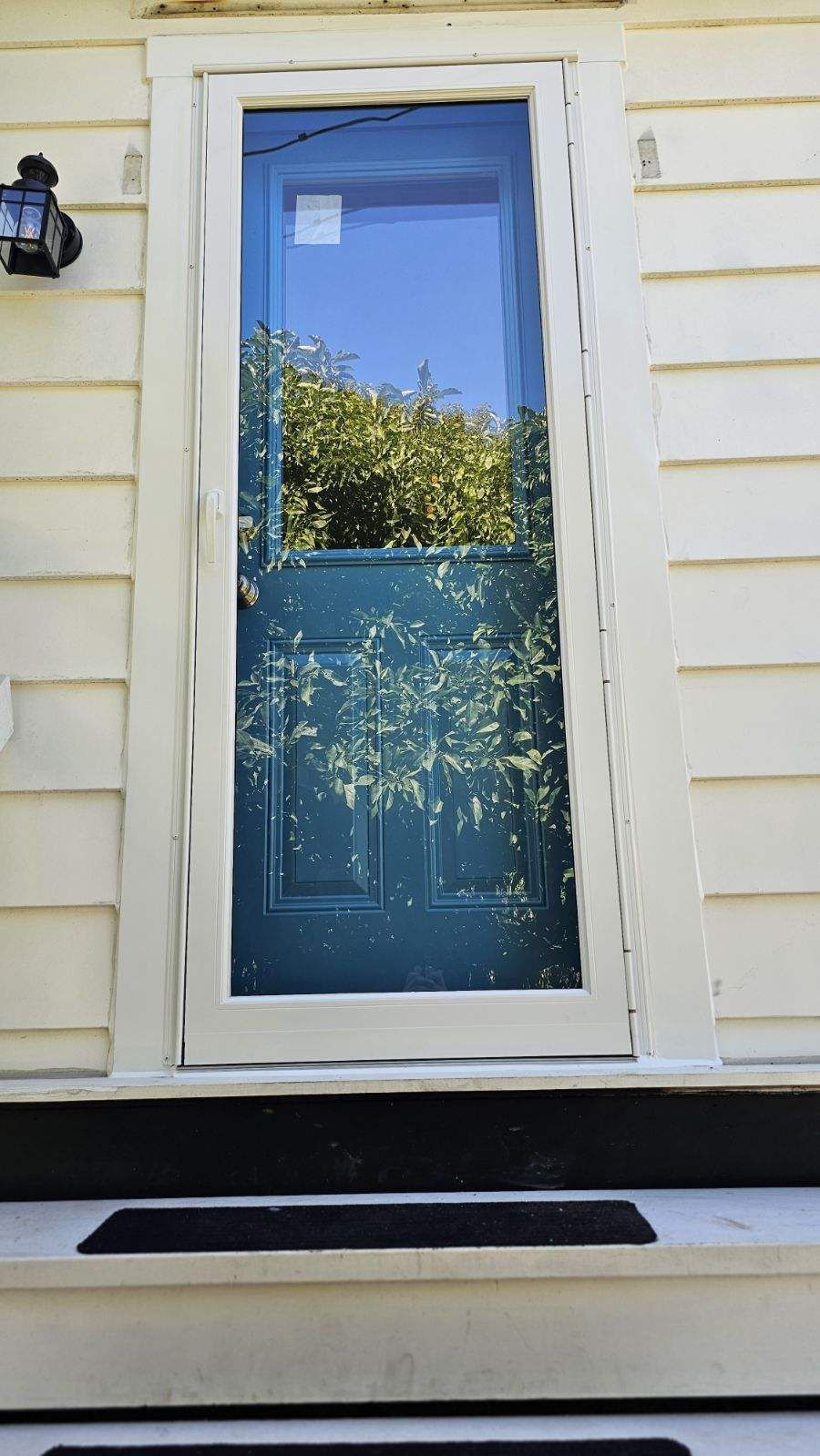 Teal door with screen, on white house. Light-colored trim. Small black doormat.