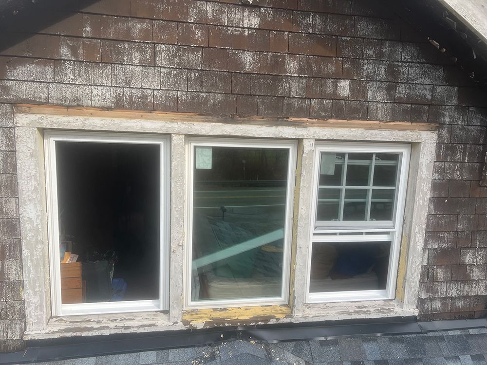 Three windows set into a brown shingled wall; the right window has grids.