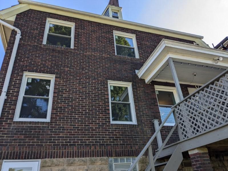 Brick building exterior with white-framed windows, small porch, and stairway, on a sunny day.