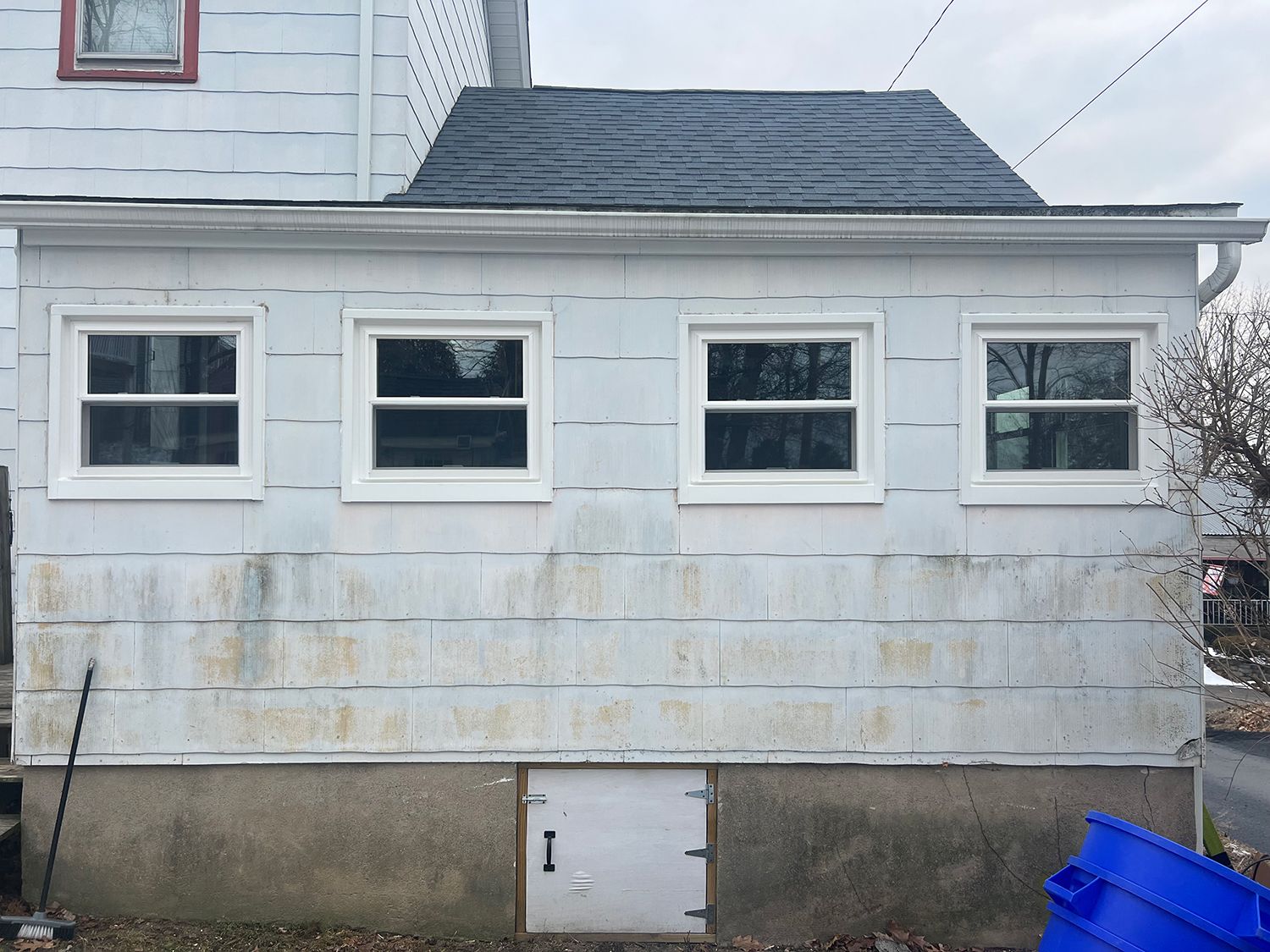 White-sided house with four windows, a small roof, and a basement door. The siding is weathered.