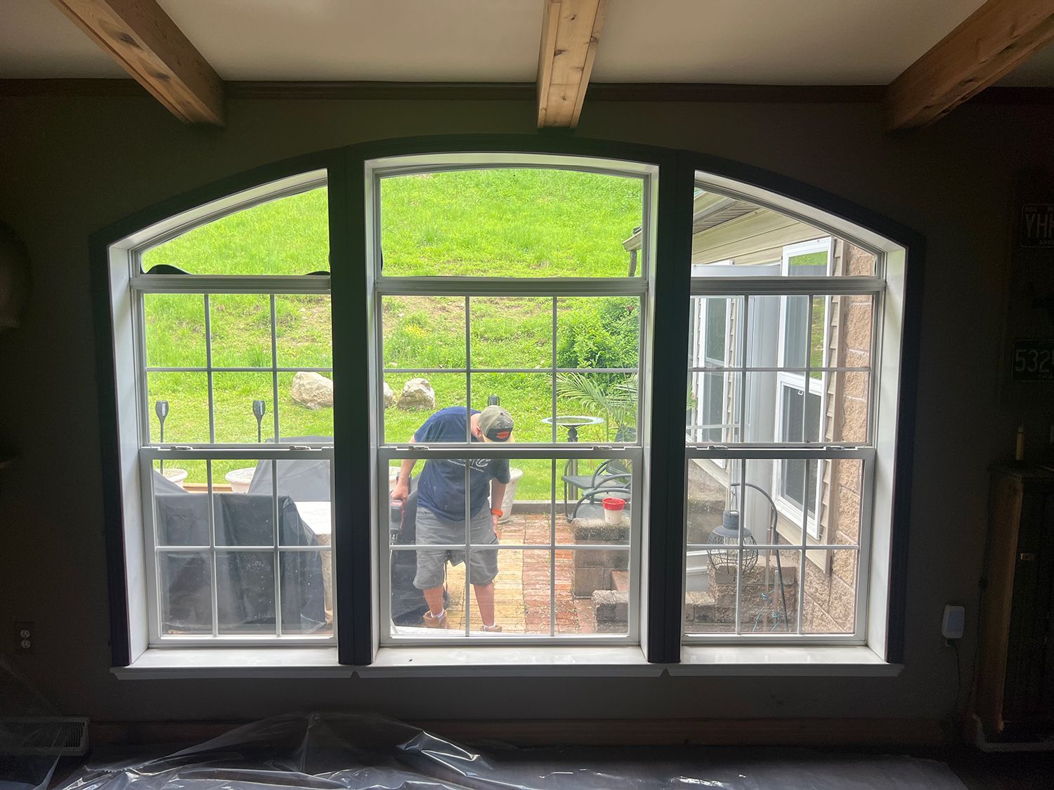 Three-pane arched window, black trim, overlooking a yard with people working outside.