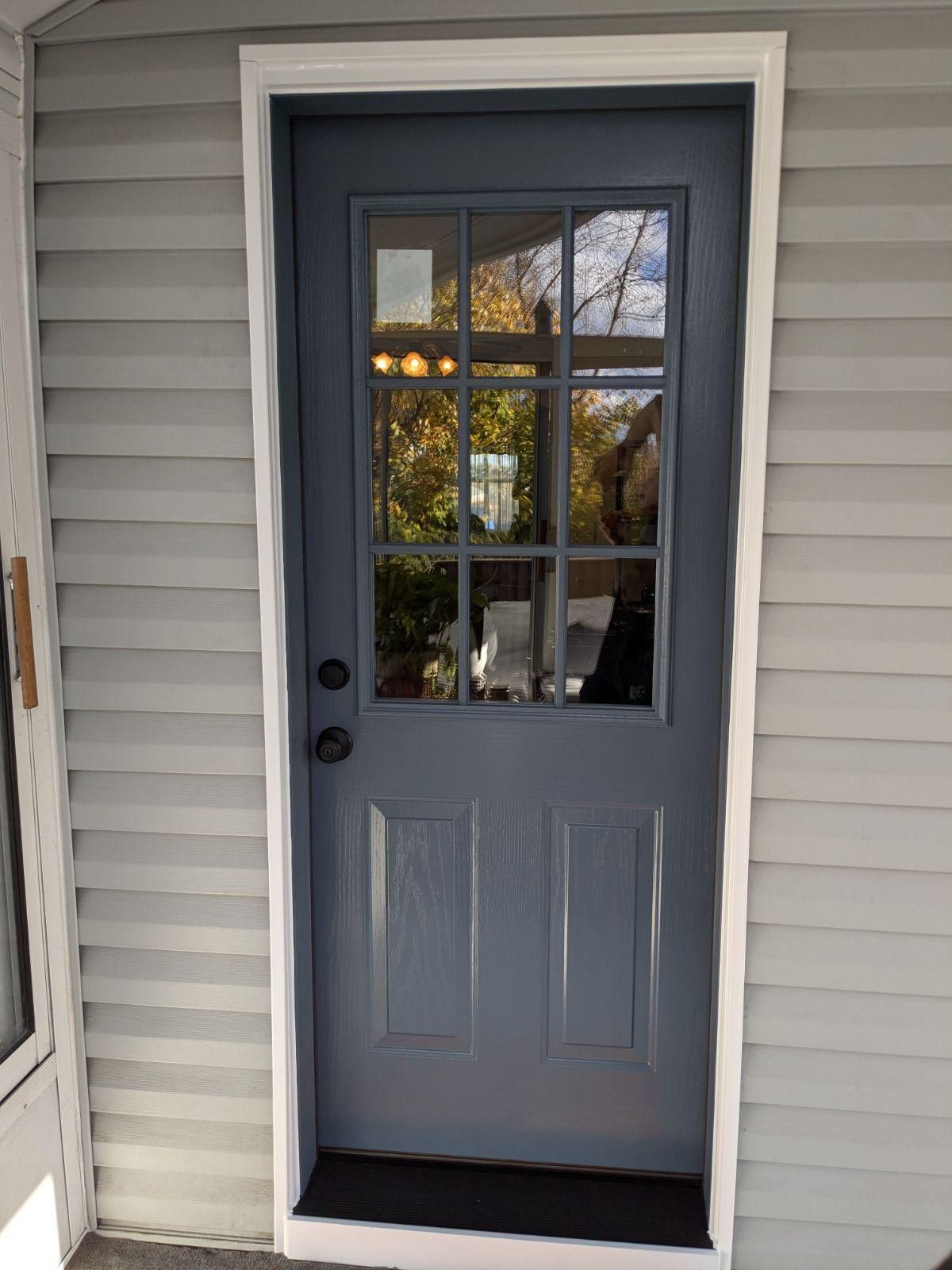 Blue door with glass panes, white trim, set in light gray siding.