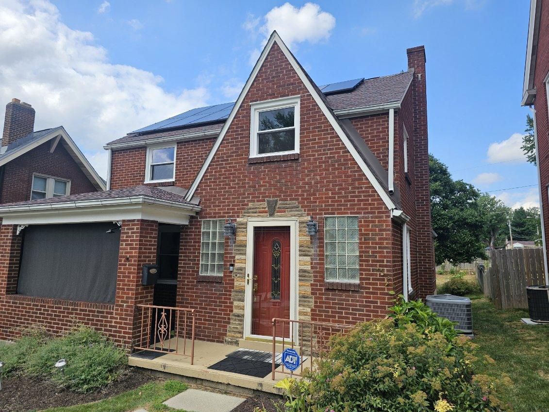 Red brick house with solar panels, a red door, and a small porch under a blue sky.