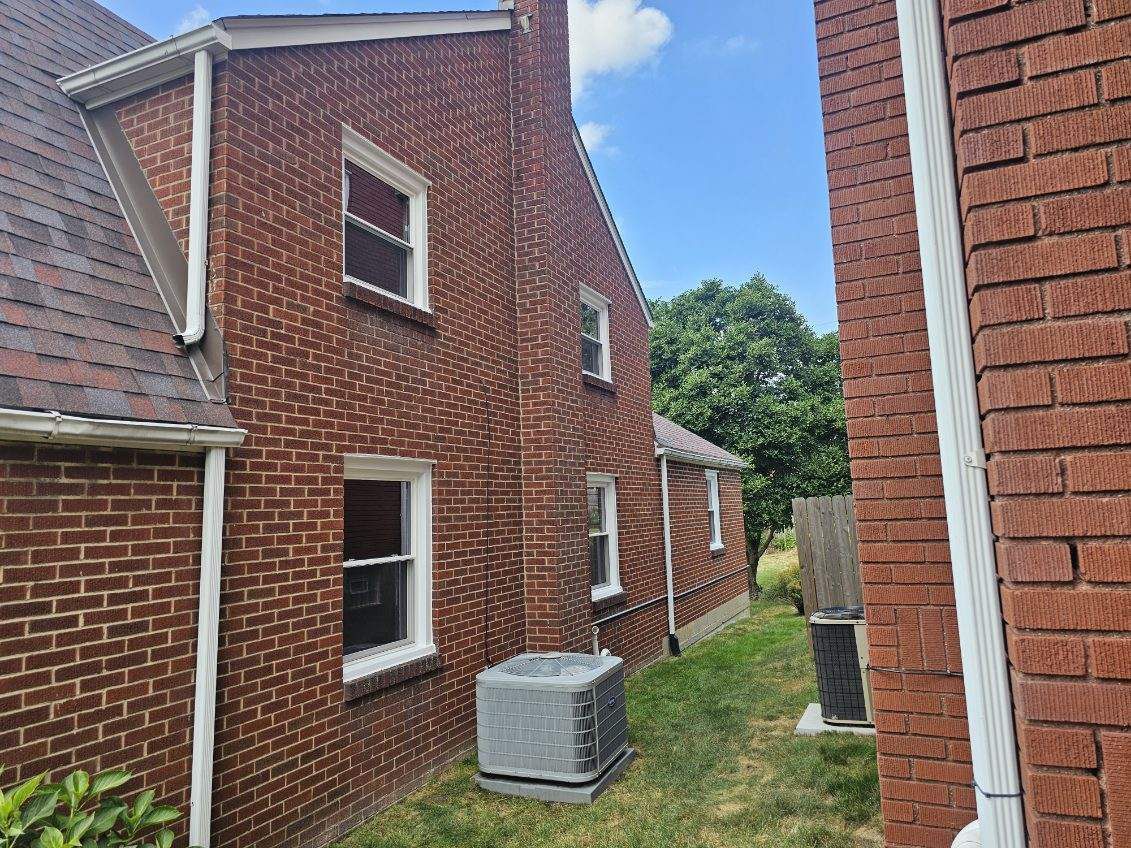 Brick house exterior with multiple windows, HVAC unit, and a chimney against a blue sky.