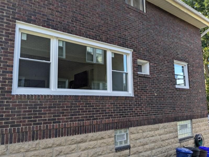 Brick house exterior with white-framed windows. Dark brick facade with light stone base. Sunny day.