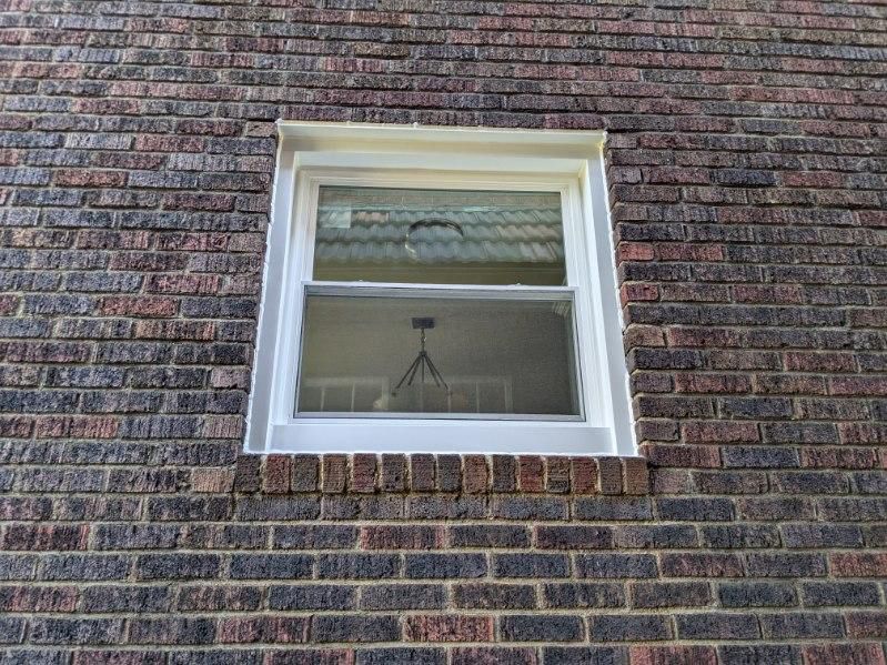 White-framed window in a red brick wall; reflecting a partially obscured interior.