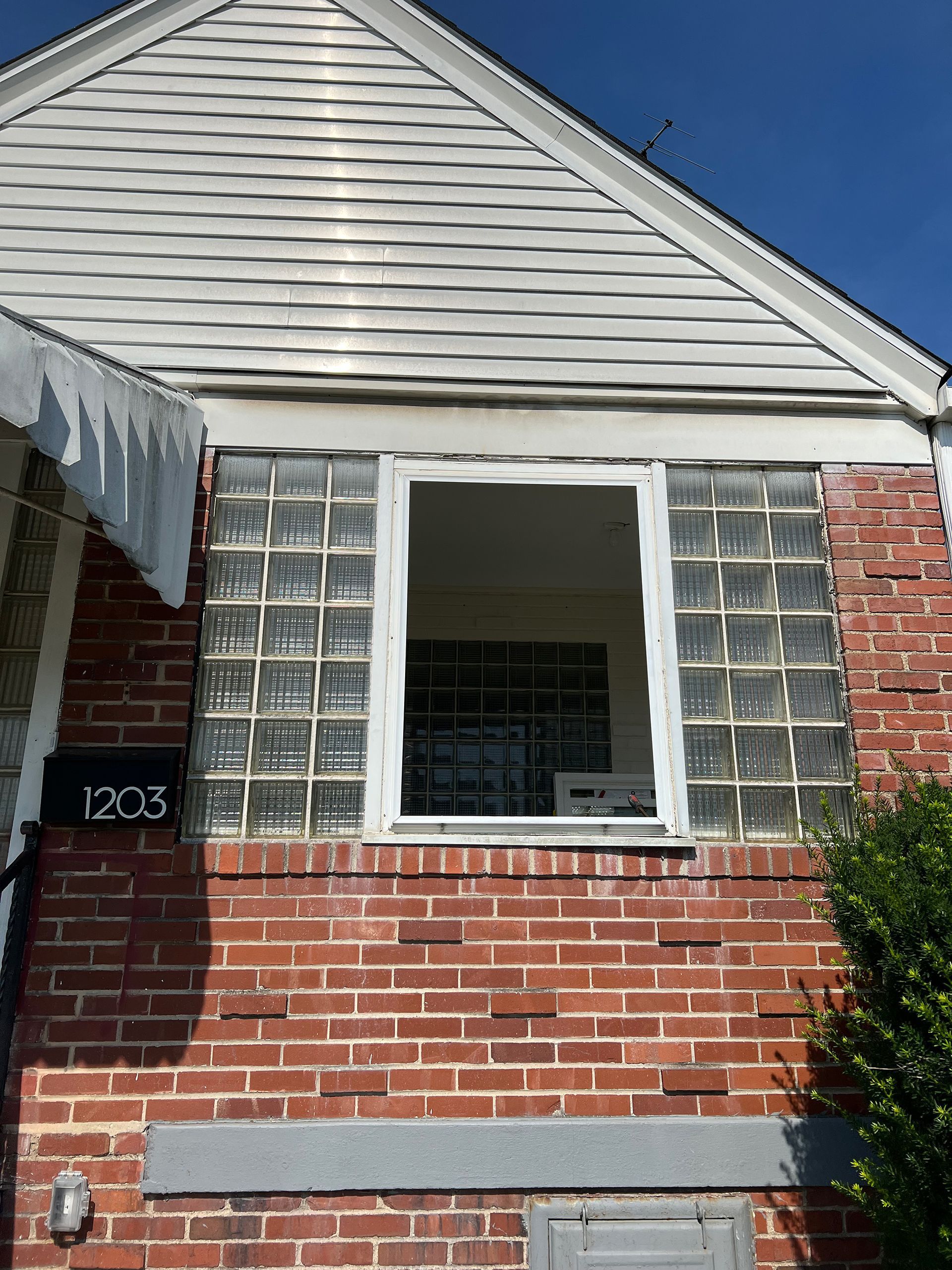 Red brick house with glass block window and missing window pane. Number 1203 visible.