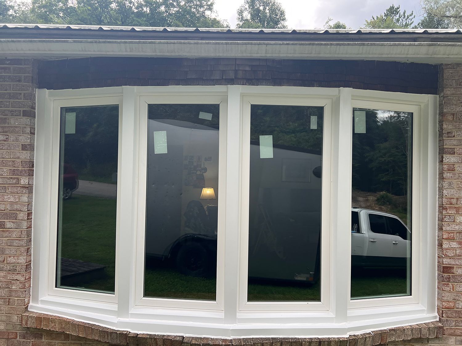 White-framed bay windows on a brick house, reflecting a street view with a white truck and greenery.