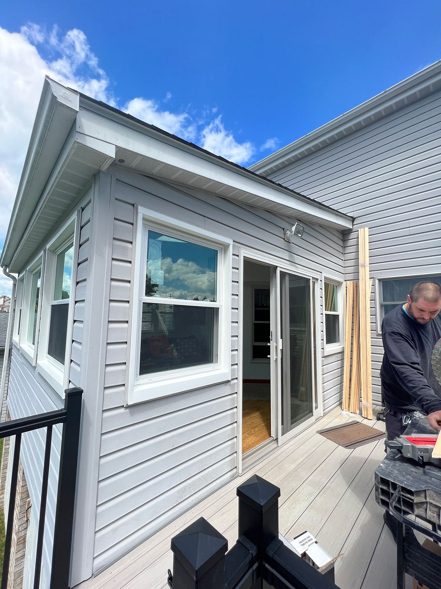 Sunroom addition on a deck, with sliding glass doors and a person working on the side.