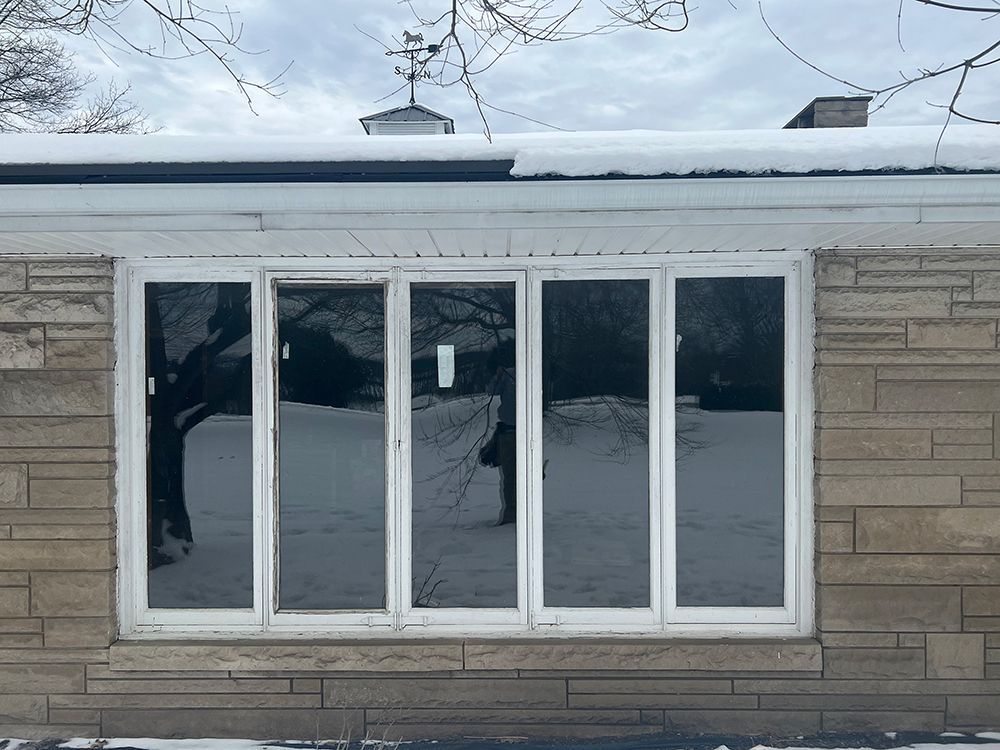 A snow-covered house with large windows reflecting trees and a cloudy sky.