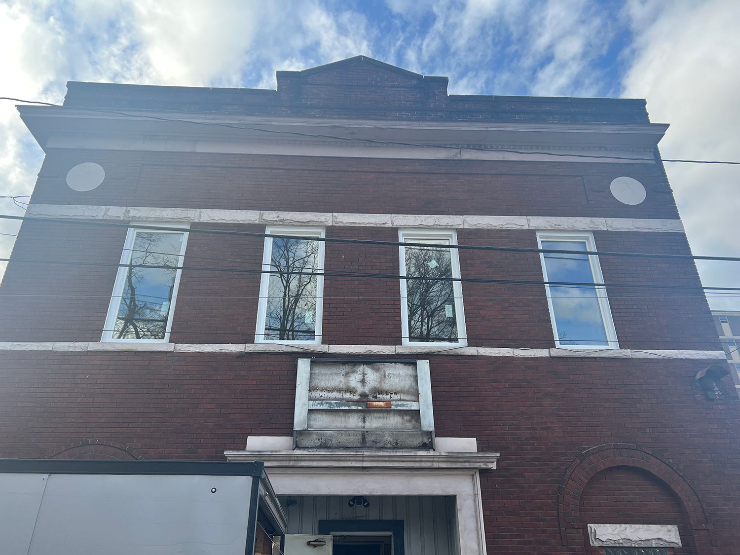 Brick building with white-framed windows and a light-colored entryway under a cloudy sky.