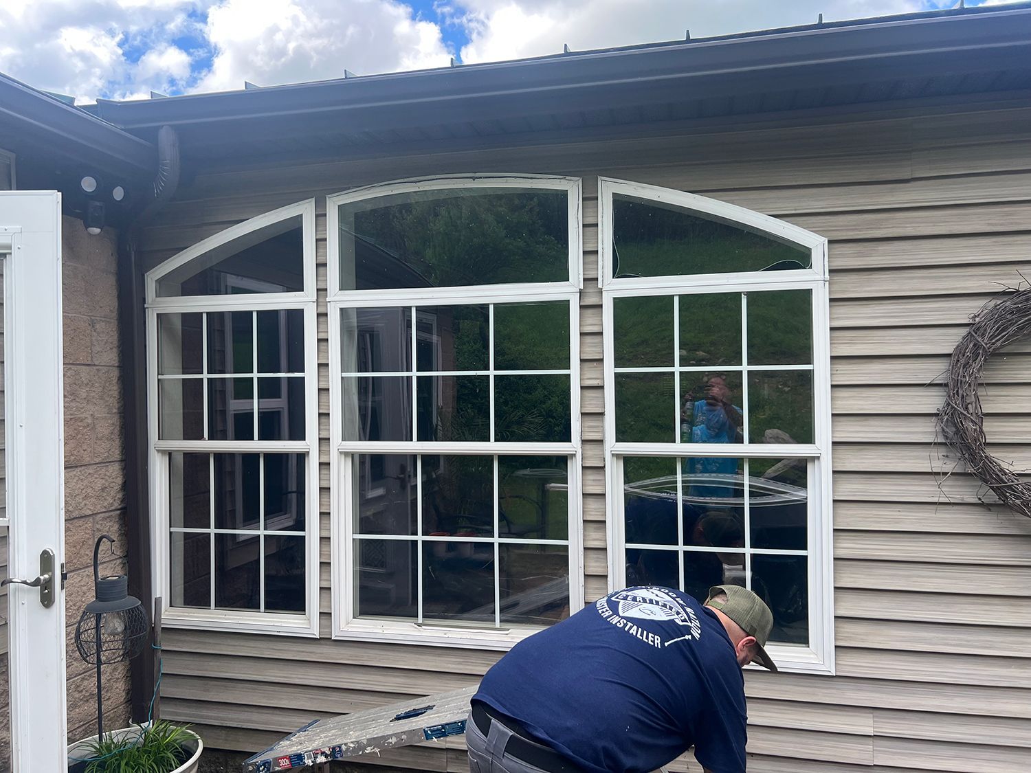 Person cleaning large windows on a wood-sided building. Arched top with white frames.