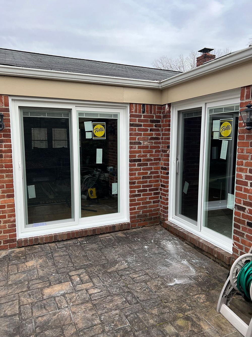 Two white-framed sliding glass doors on a brick building with a brick patio.