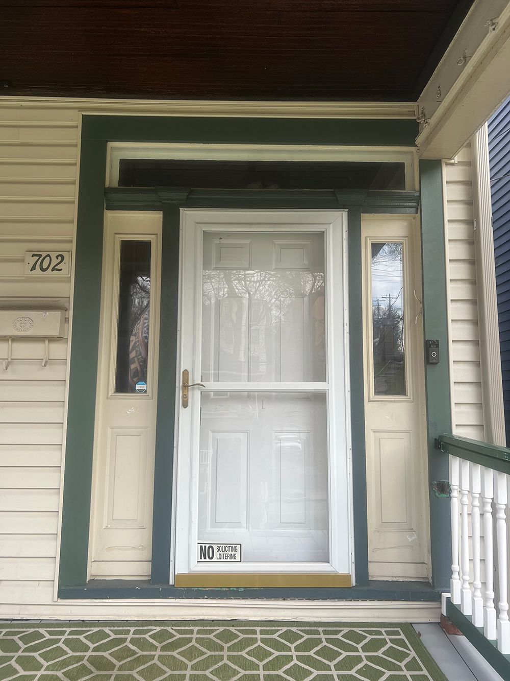 Front door of house with screen door, sidelights, green trim, and porch.