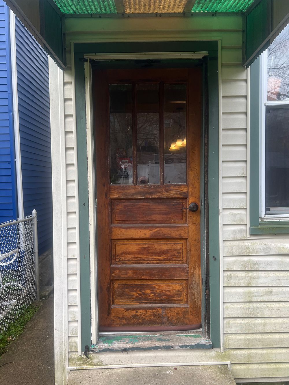 Wooden door with glass panes, weathered wood, green trim, under a green awning.