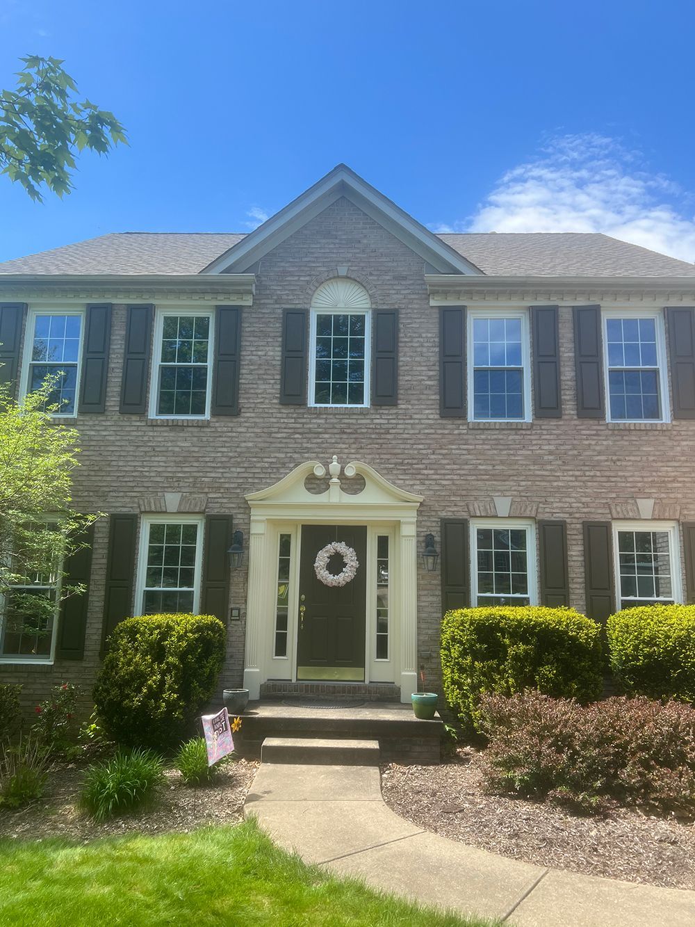 Two-story brick house with brown shutters, white trim, front door with wreath, and a walkway.