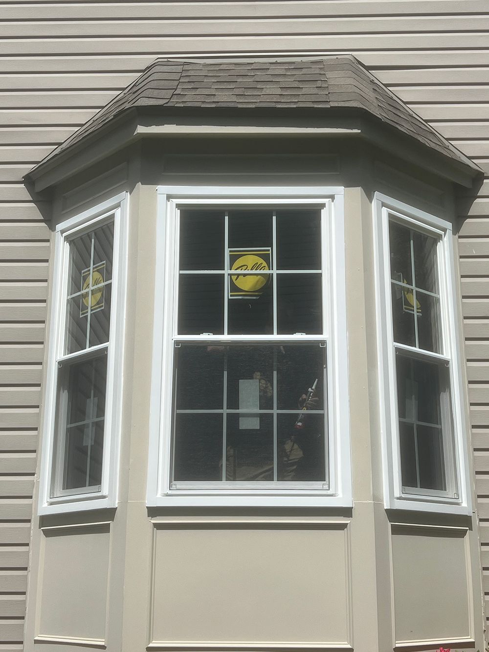 A bay window with white frames and a tan exterior. The windows have a grid pattern and are covered with protective material.