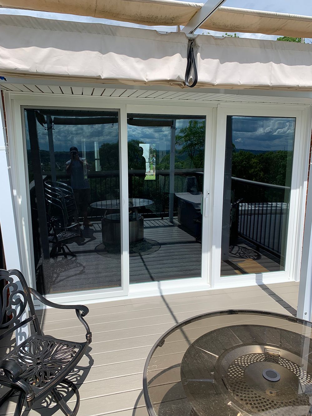 Sliding glass doors on a deck with a wrought iron chair and table, under an awning.