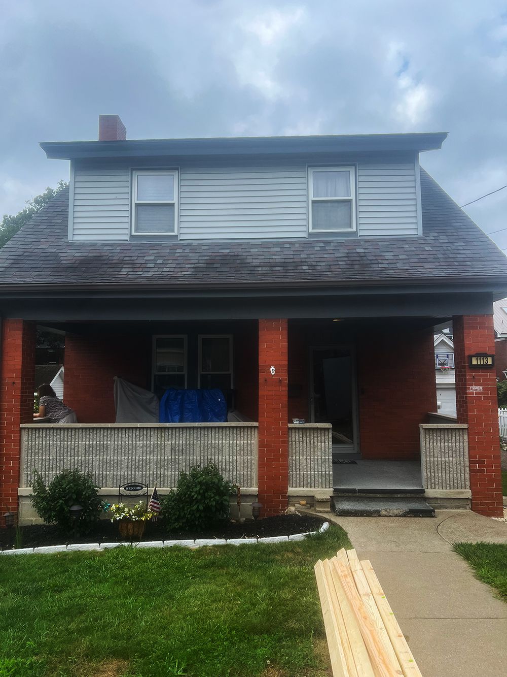 Brick house with porch and gray siding on the second story under a cloudy sky.