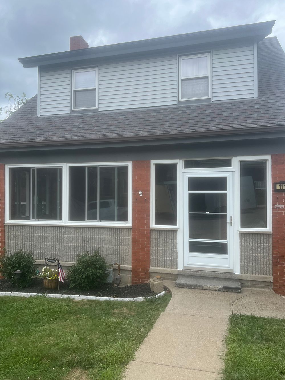 Two-story house with red brick and gray siding; walkway leads to a white door.
