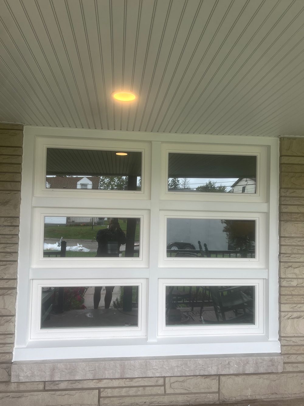White-framed window with six panes, set in a stone wall. A person is reflected in the glass.
