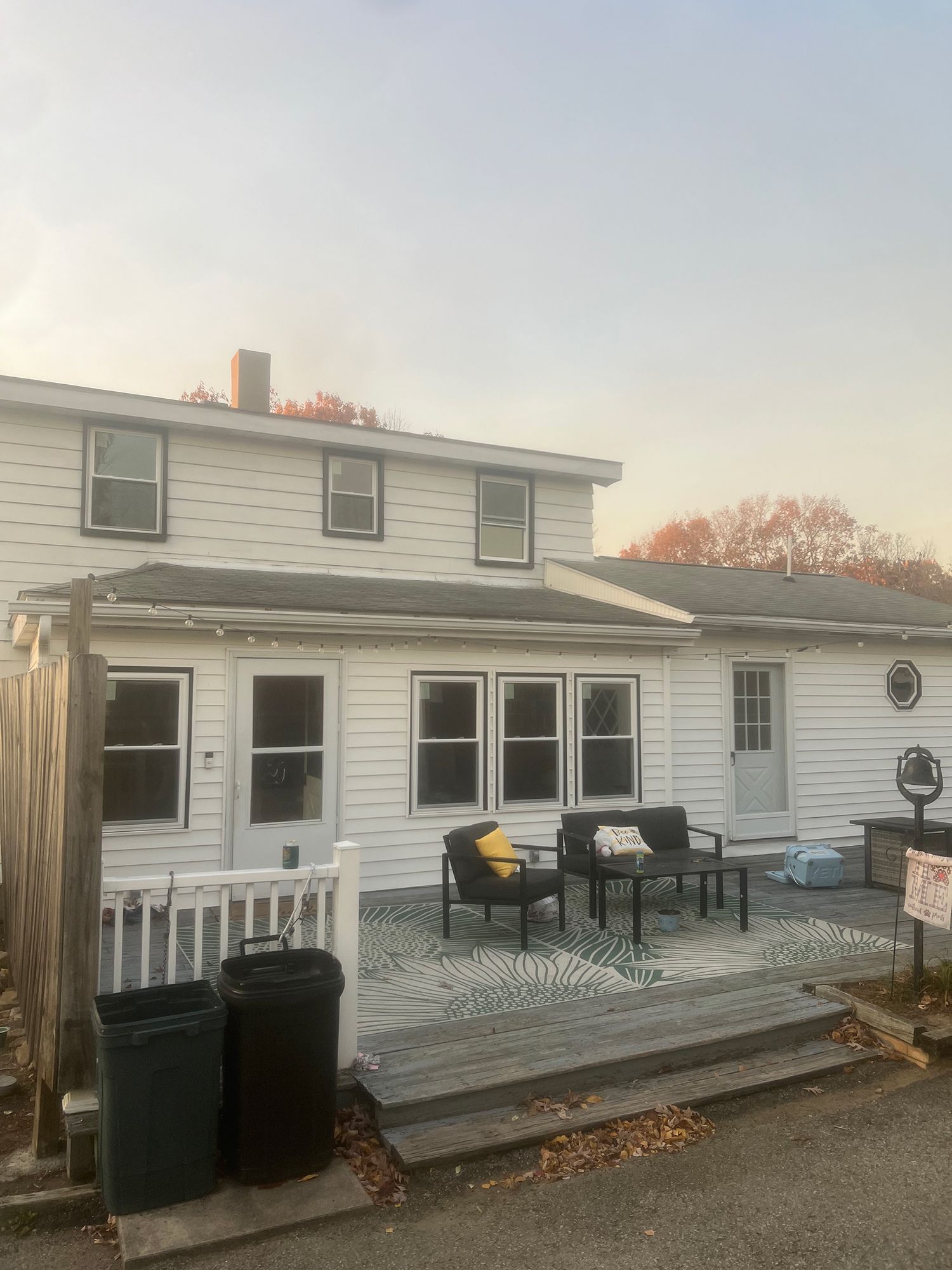 White two-story house with deck and outdoor seating under an autumn sky.