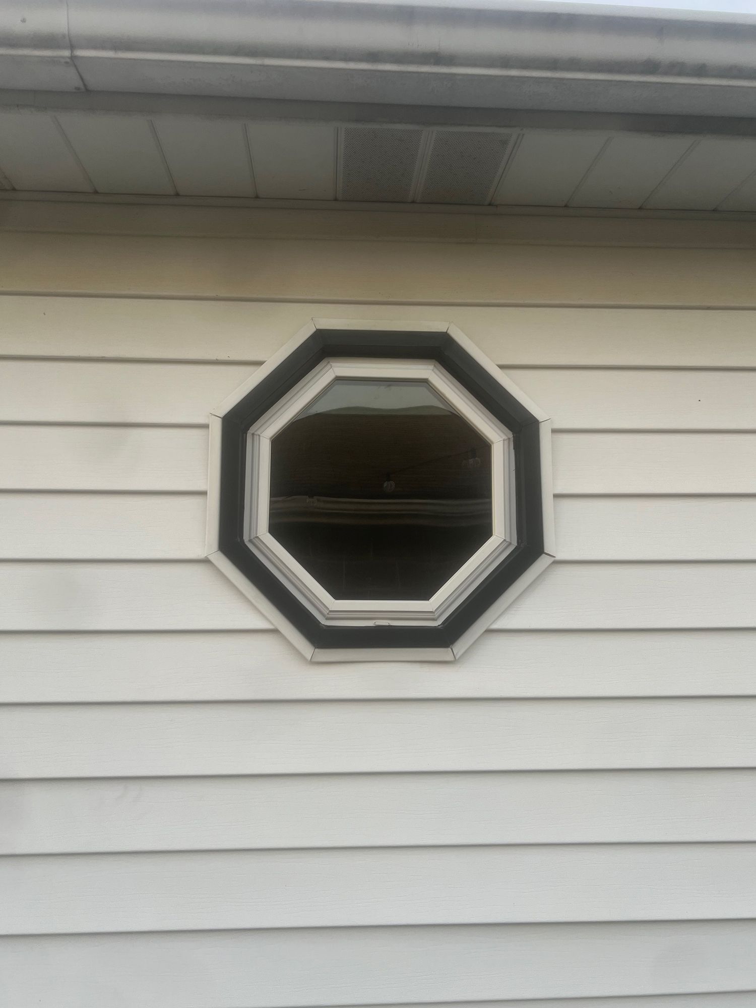 Octagonal window with black and white trim on white siding.
