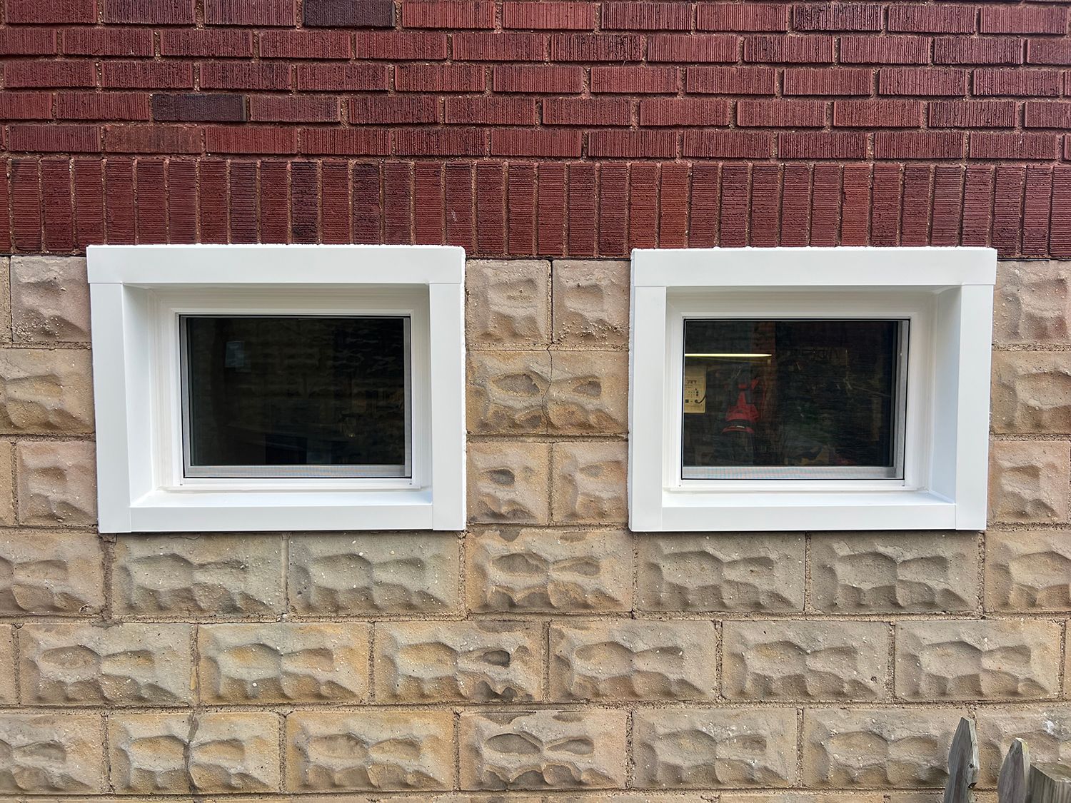 Two square windows with white frames on a brick building. The upper brick row is red, and the lower row is tan.