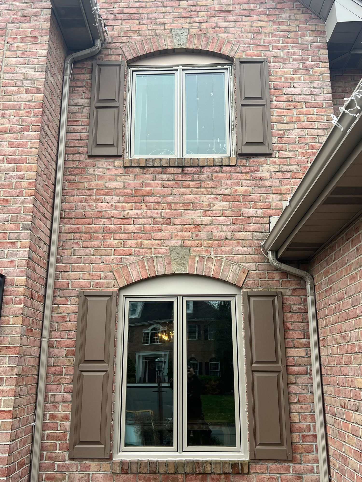 Red brick building with two windows and brown shutters.