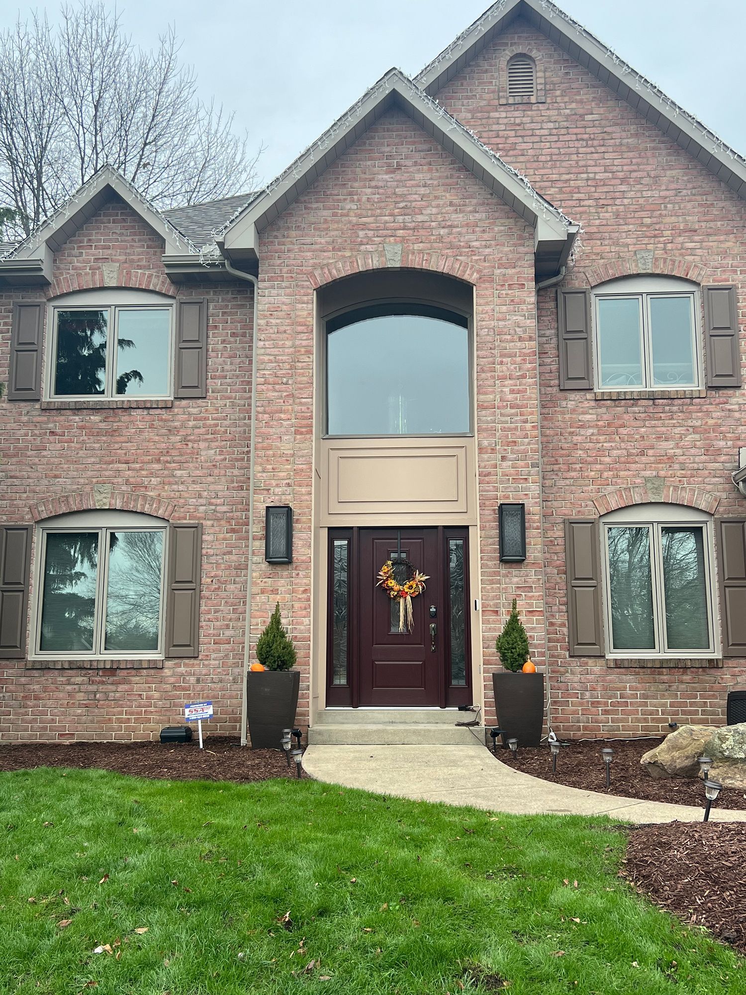 Brick house with maroon door, shutters, and window frames, decorated for fall with pumpkins and wreath.