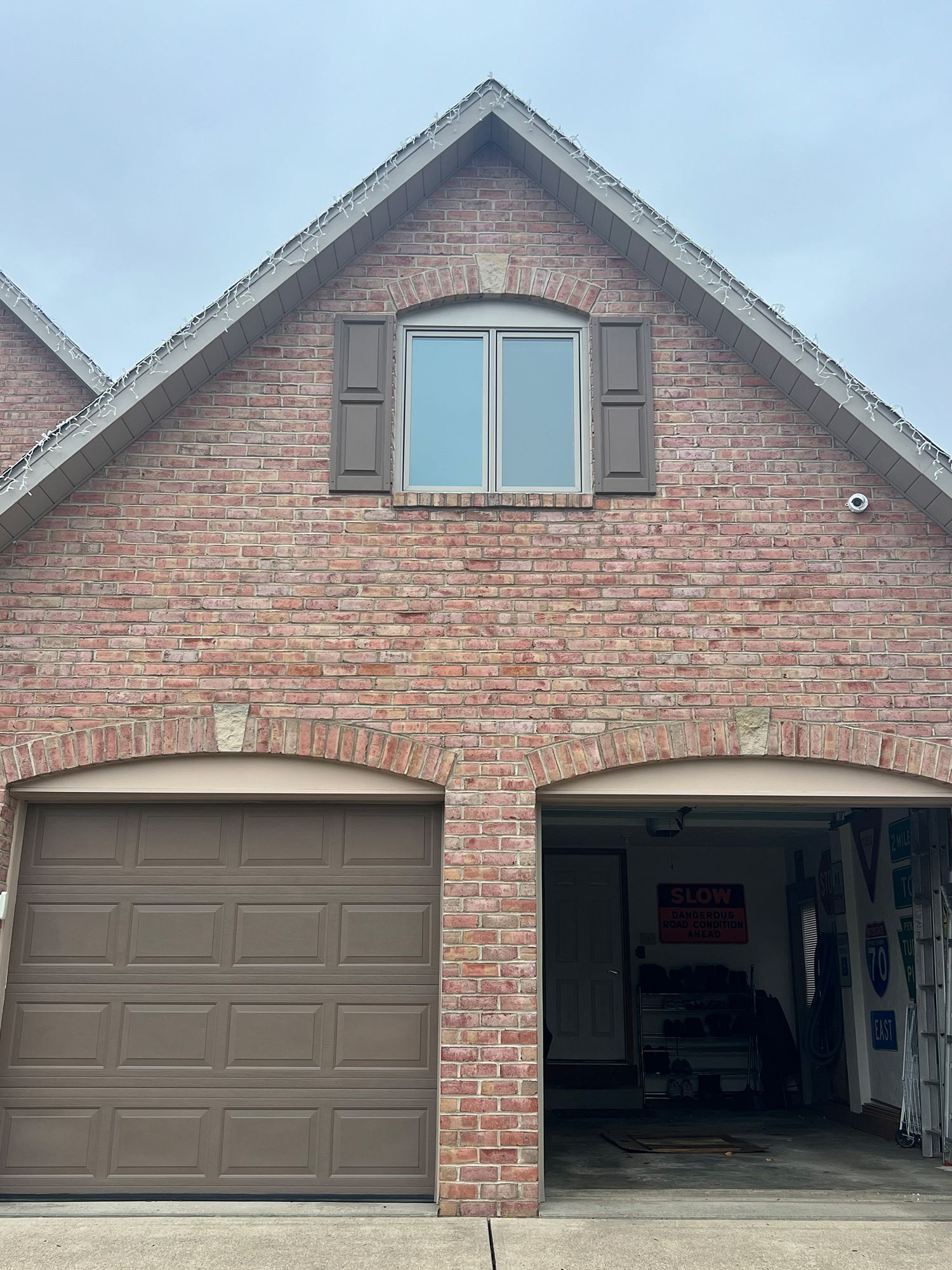 Brick house with two garage bays, brown doors, and a second-story window with shutters.