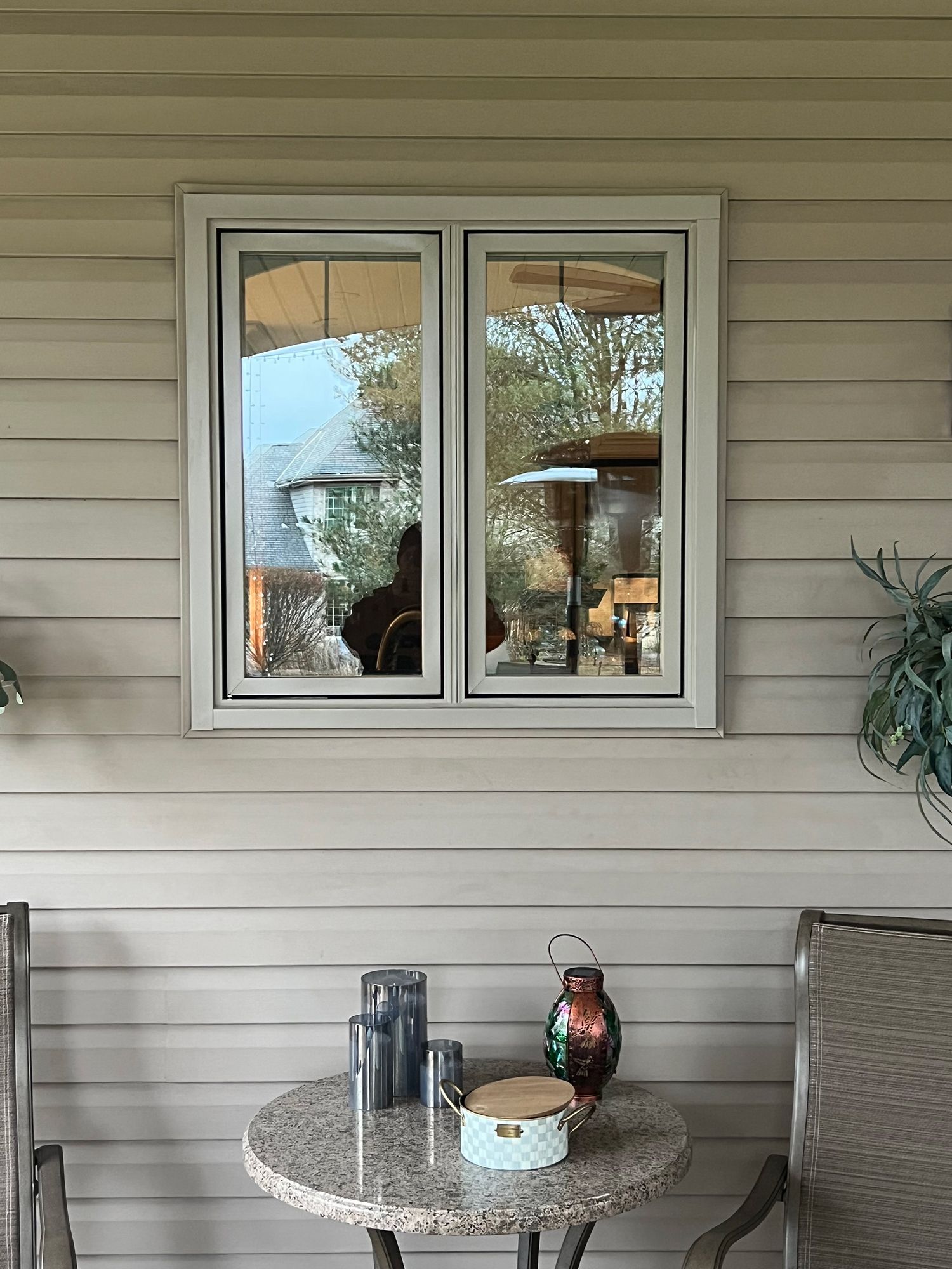 Window in a cream-colored siding. A small table with decorations in front of it.