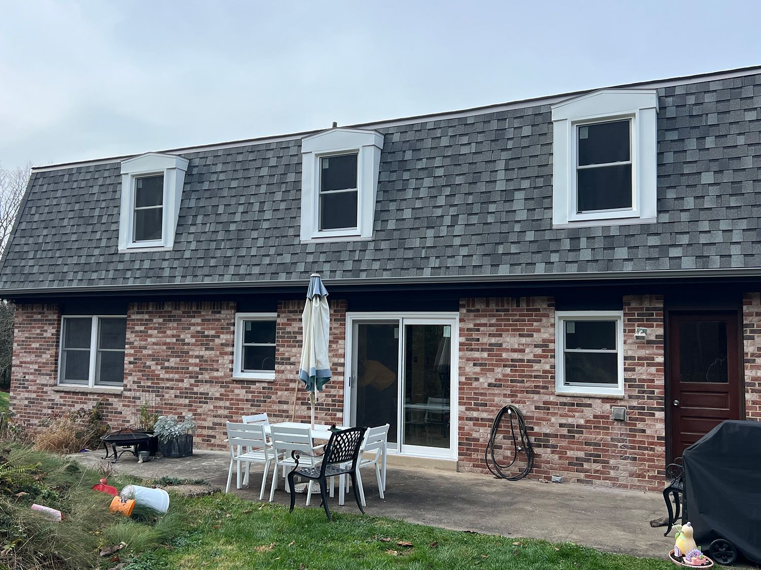 Brick house with three dormers, a sliding glass door, and outdoor seating on a patio.