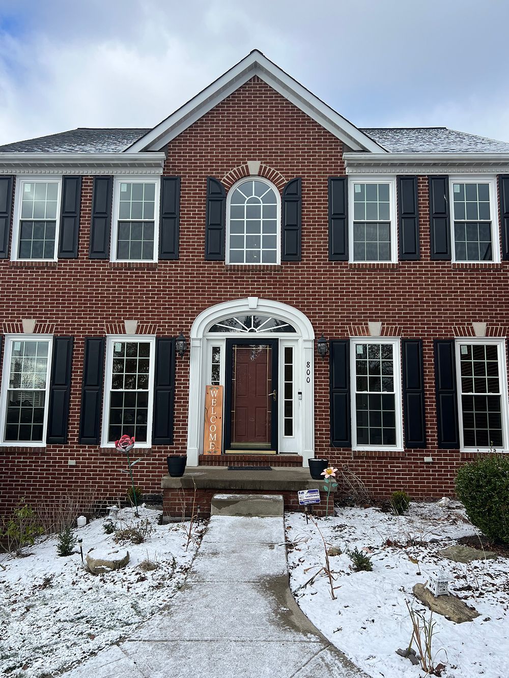 Brick house with black shutters, white-trimmed windows, and a snowy front yard.
