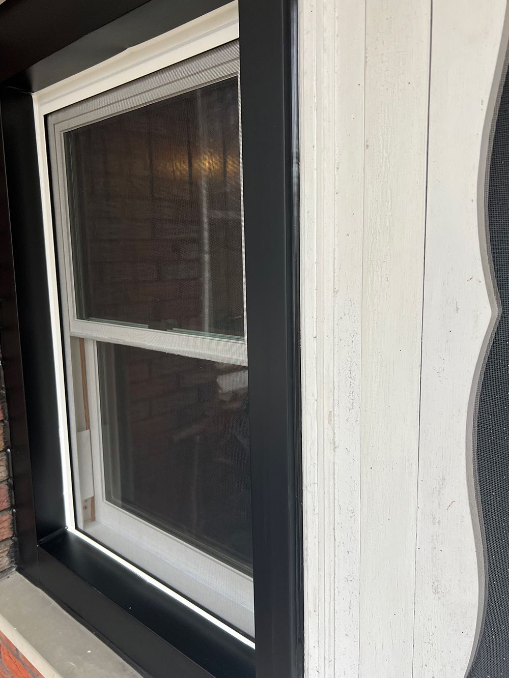 Black framed window with white trim. A window screen covers the inside, set outdoors.