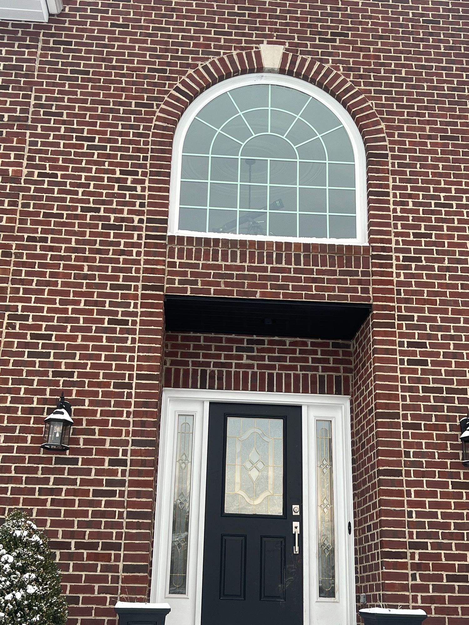 Brick facade with arched window, black door, and snow.