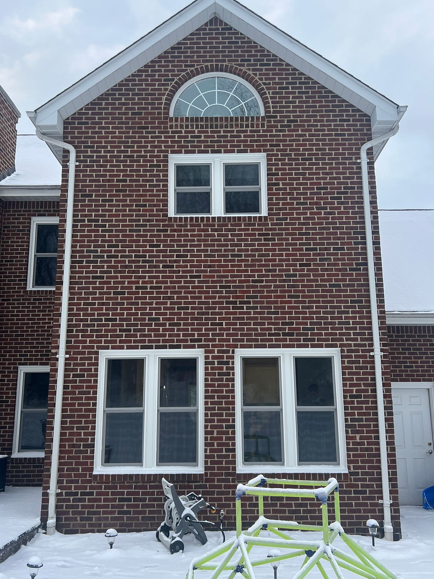 Brick house exterior with white trim. Windows, arched window, snow, and green play structure.
