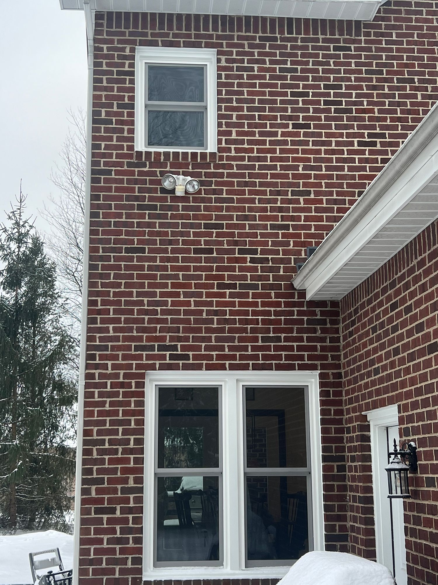 Red brick house exterior with two windows, snow, and a security camera.