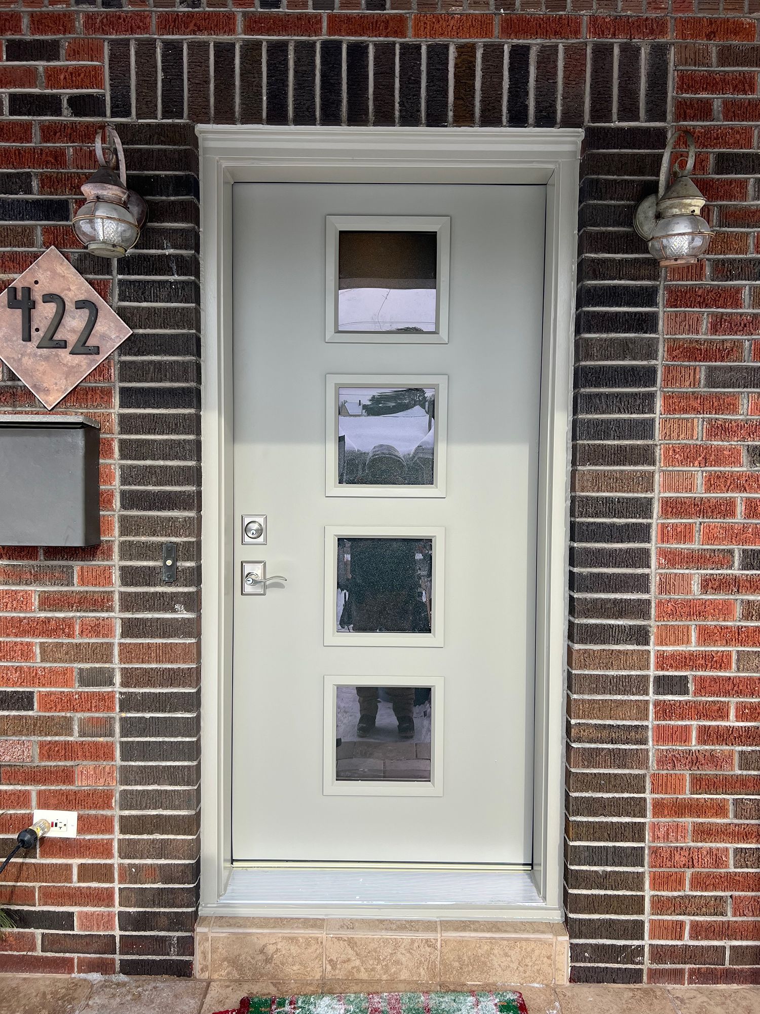 Off-white door with four glass panels, surrounded by red brick. Two wall lamps and address 122 are visible.