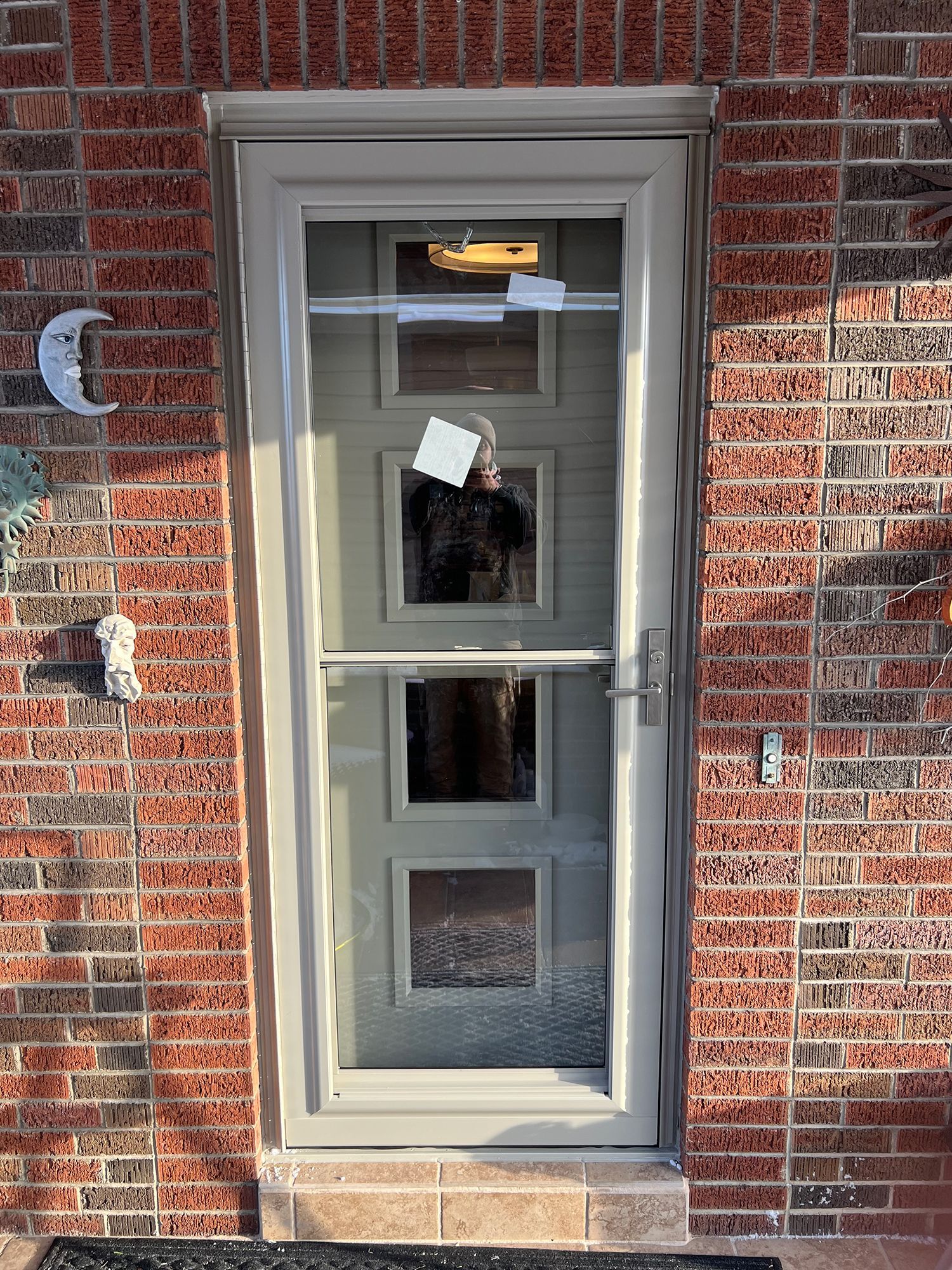 Beige screen door with glass panels set in a red brick wall.