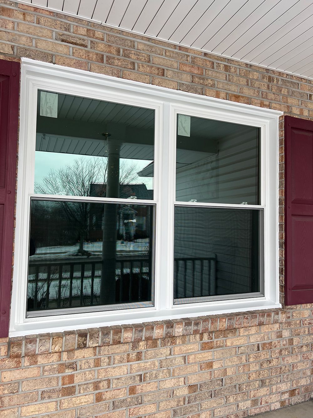 White-framed double window on a brick building, burgundy shutters on each side, overcast daylight.