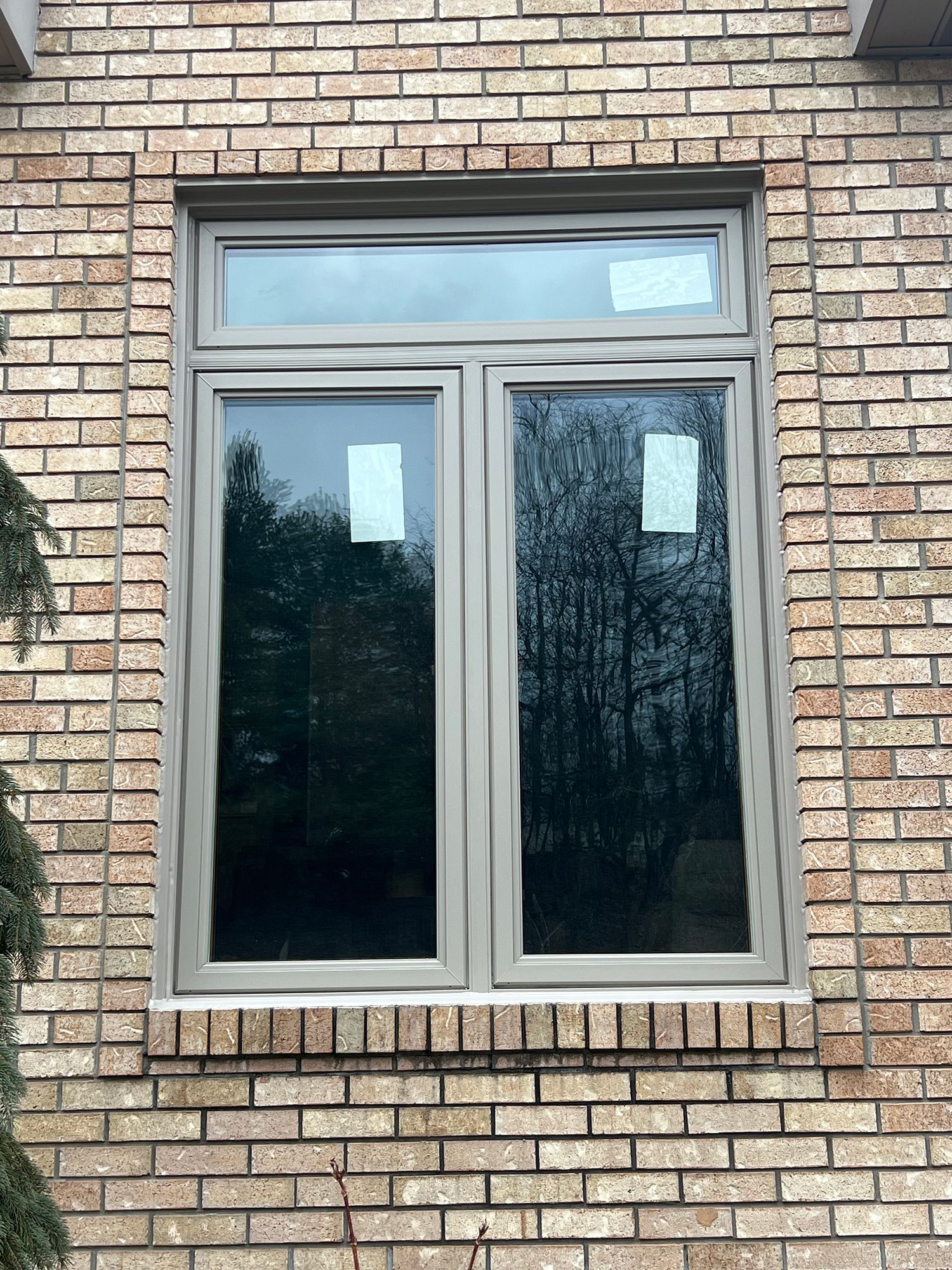 A brick building with a gray window. The window is divided into three sections, with two large lower panels.