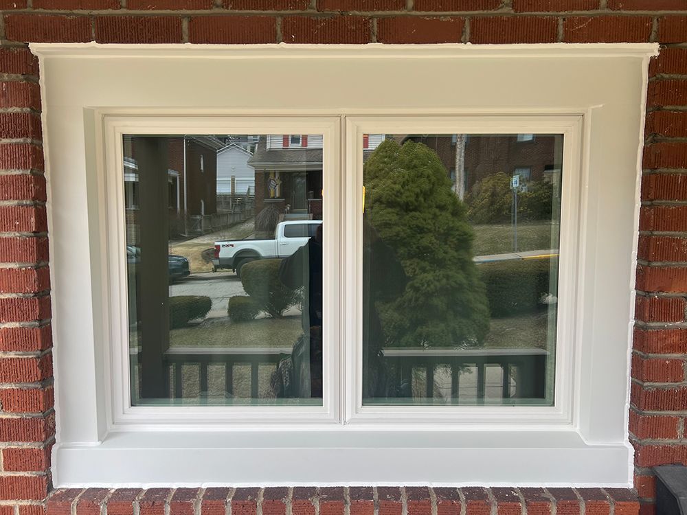 White-framed double window with decorative trim against red brick exterior.