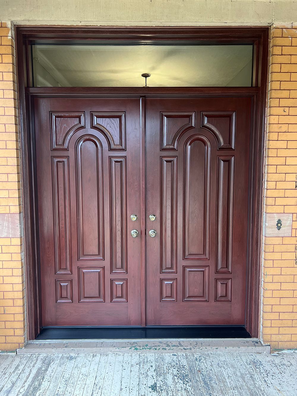 Double brown wooden doors with arched panels, flanked by brick walls.