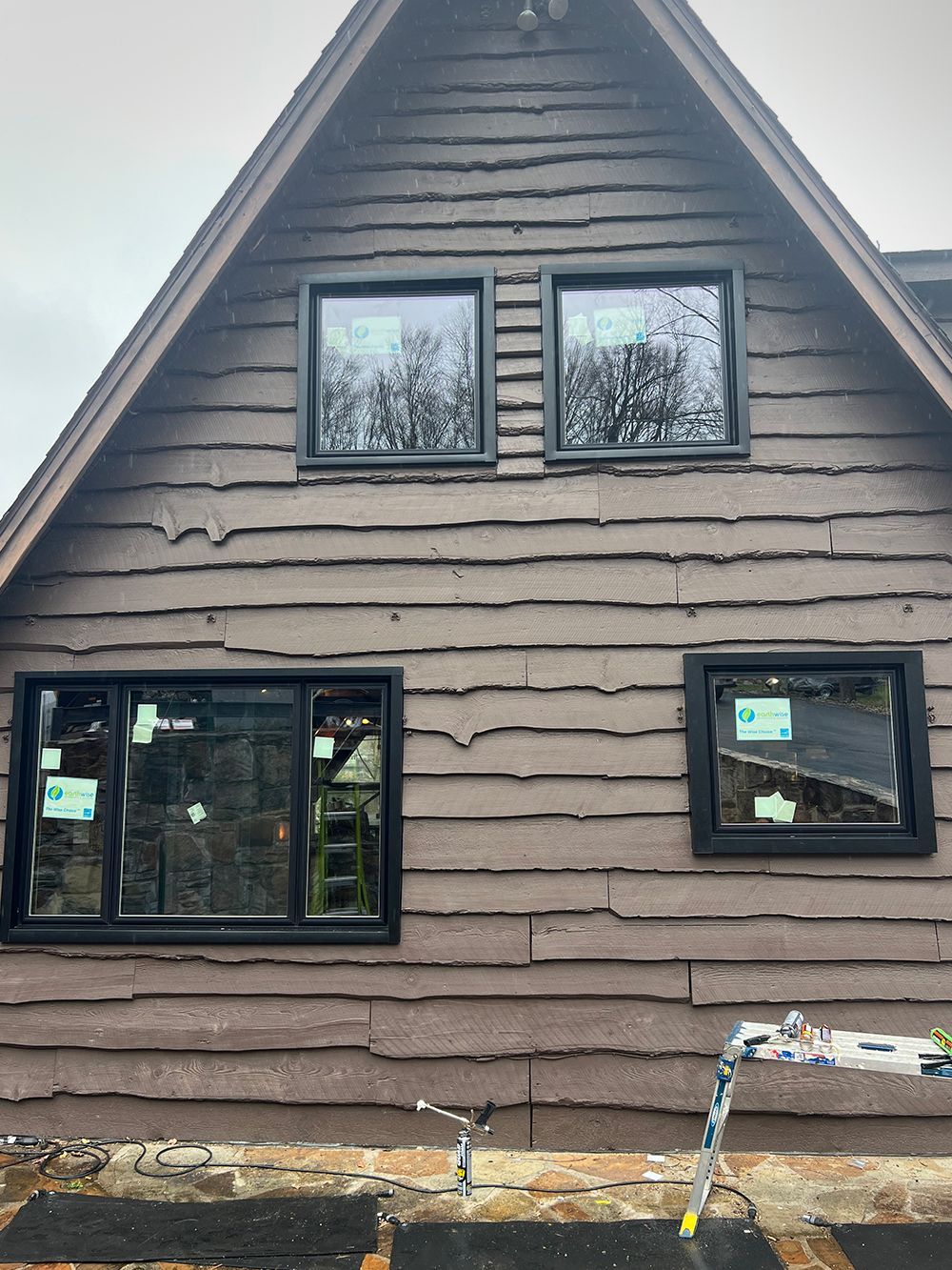 Brown house exterior with four black-framed windows. The wood siding is weathered.