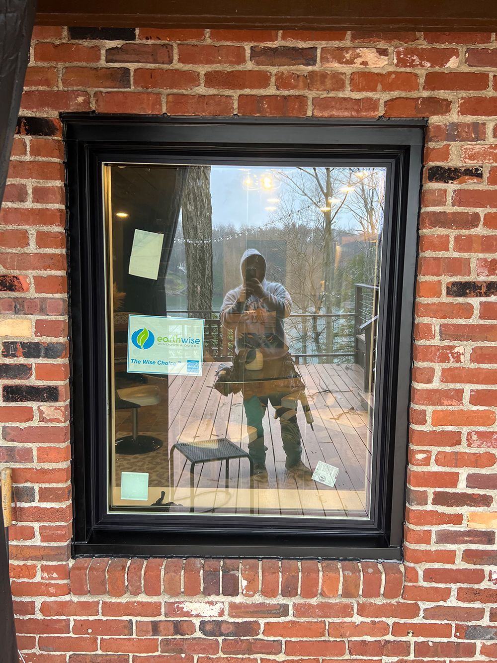 Window with black frame in a brick wall, reflecting a person and outdoor deck.
